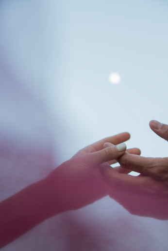 Hands reaching toward one another under a pale moon